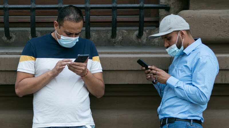Dos hombres con mascarillas mirando sus teléfonos móviles