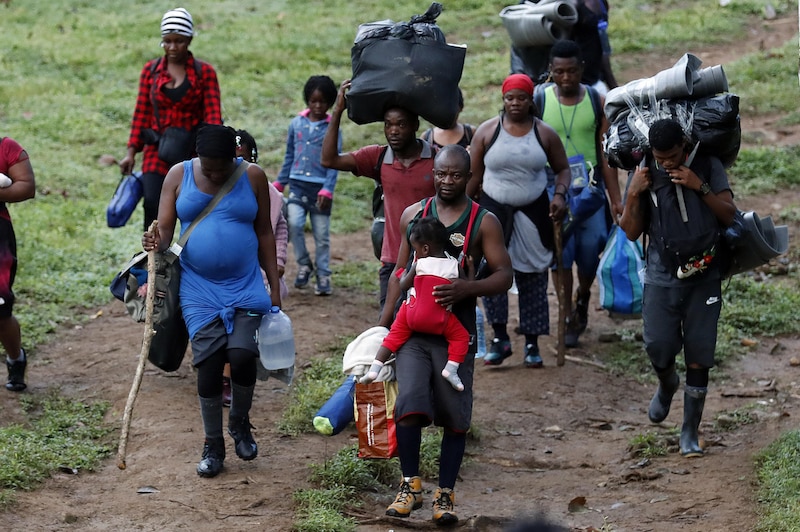 Migrantes haitianos caminan en grupo por un camino rural.