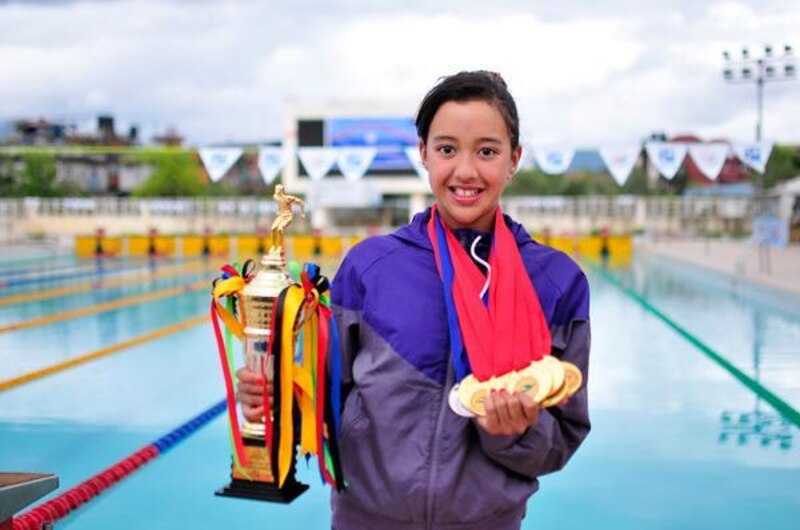 Joven nadadora sostiene un trofeo y medallas