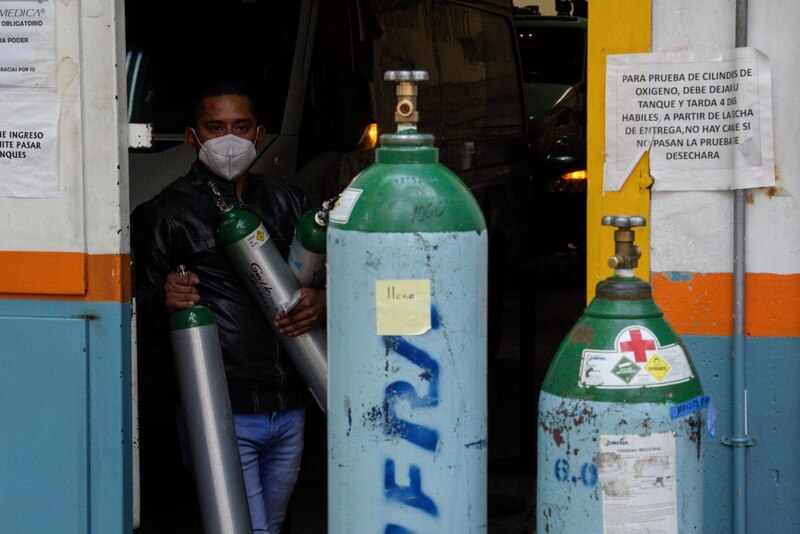 Un hombre con una mascarilla facial sostiene dos tanques de oxígeno.
