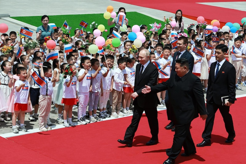 Kim Jong-un y Vladimir Putin caminan por una alfombra roja mientras los niños los saludan con banderas y globos