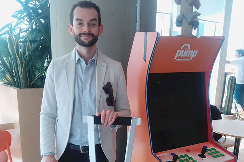 Un hombre sonríe junto a una máquina arcade.