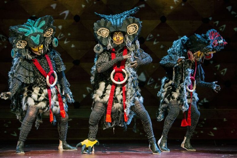 Tres bailarines con trajes de búho realizan una danza contemporánea sobre un escenario de madera.