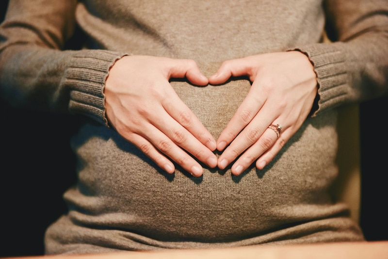 Mujer embarazada con sus manos sobre su vientre formando un corazón con los dedos