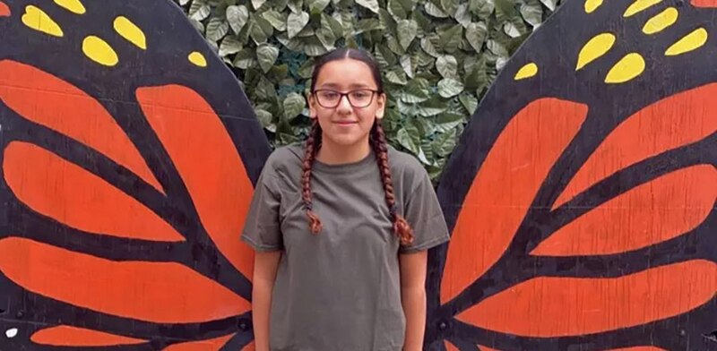 Niña posando con alas de mariposa pintadas en una pared