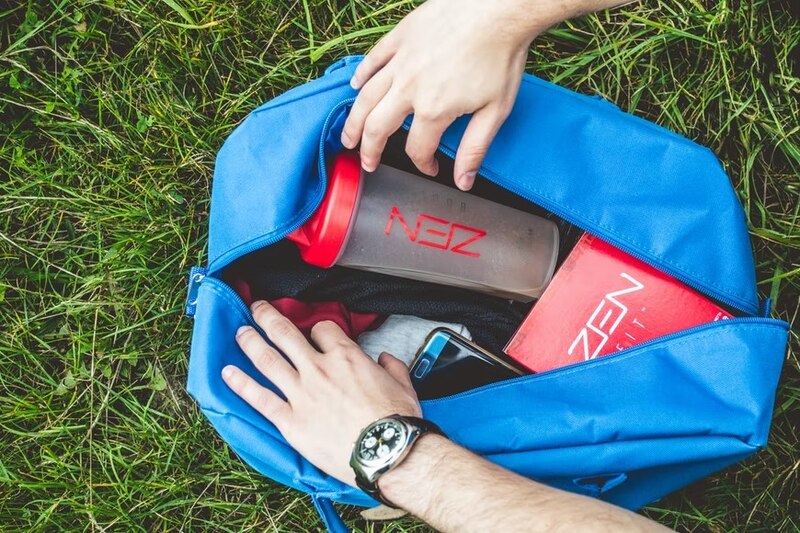 Mochila deportiva azul abierta con ropa, teléfono y botella de agua