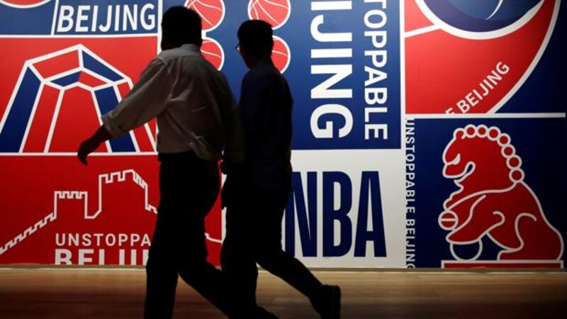 Dos hombres caminan frente a un mural de la NBA en Pekín