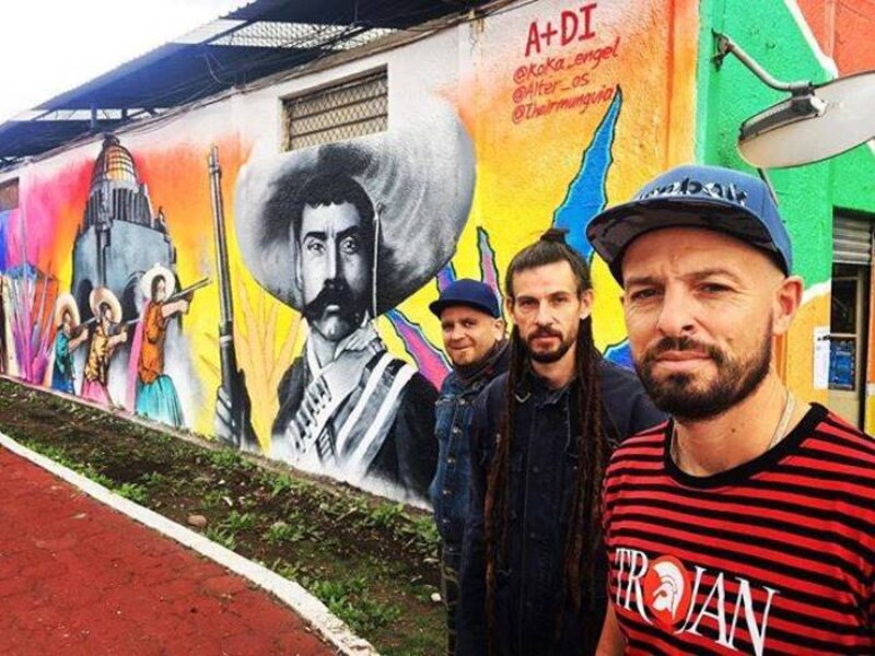 Tres hombres parados frente a un mural de Emiliano Zapata