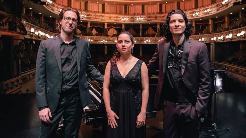 Tres músicos sonríen y posan para una foto en un teatro.
