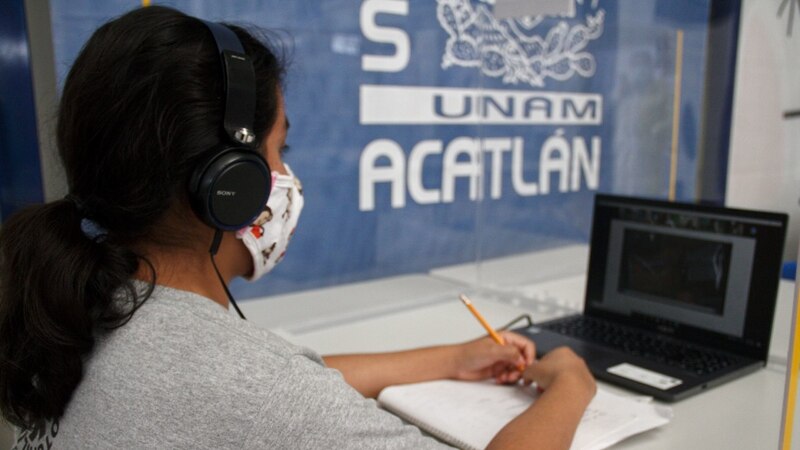 Estudiante universitaria con cubrebocas tomando apuntes en clase en línea