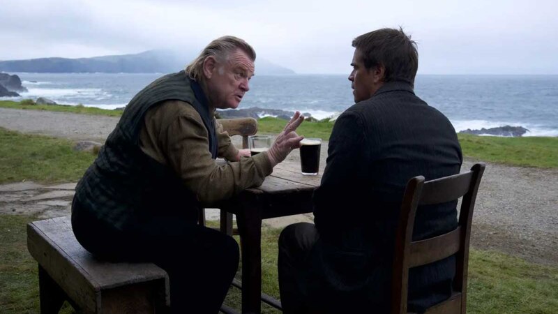 Dos hombres están sentados en una mesa de un bar al aire libre, mirando al mar y hablando.