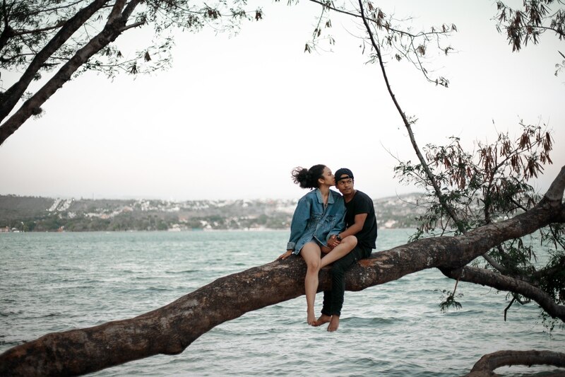 Pareja sentada en la rama de un árbol sobre el agua