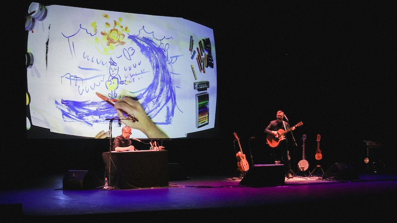 Un artista dibuja en una pantalla mientras un músico toca la guitarra