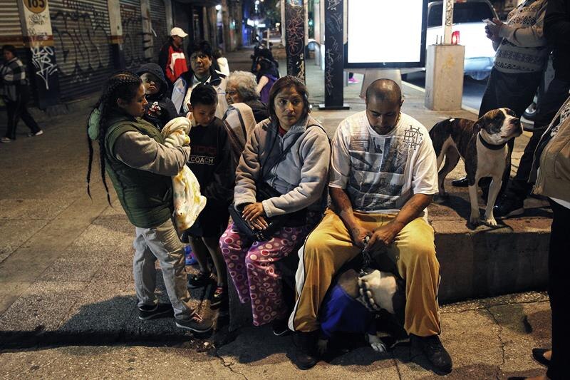 Un grupo de personas, incluyendo niños, esperan en una calle de la ciudad.