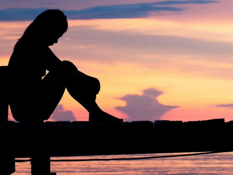 Mujer triste sentada en un muelle al atardecer