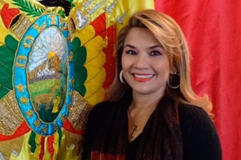 La Presidenta de Bolivia, Jeanine Áñez, sonríe ante la bandera de su país.