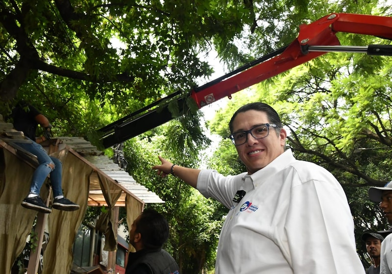 Luis Mendoza vestido de camisa blanca, apuntando a grúa con trabajadores de limpieza