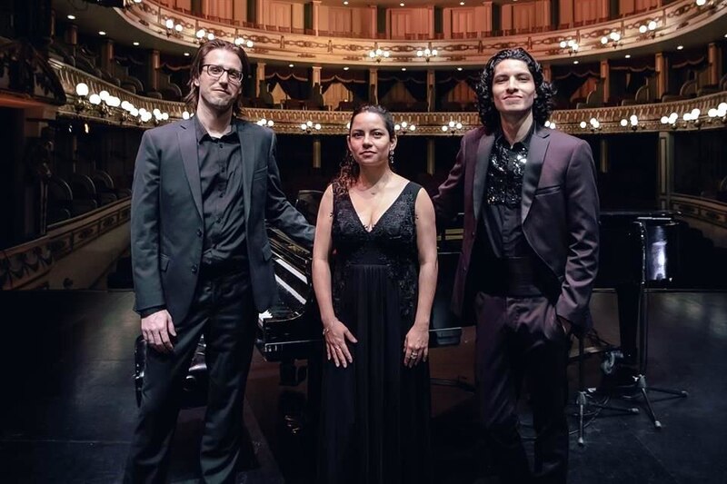 Tres músicos vestidos de negro posan para una foto en un teatro.