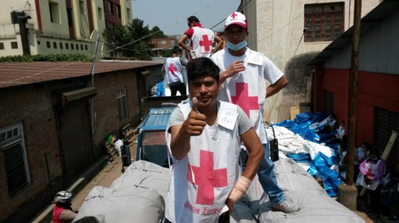 Un trabajador de la Cruz Roja nepalí sonríe y hace un gesto de aprobación con el pulgar hacia arriba mientras se encuentra en la parte trasera de un camión cargado de suministros de ayuda.