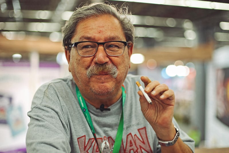 Un hombre con bigote y gafas sostiene un cigarrillo.