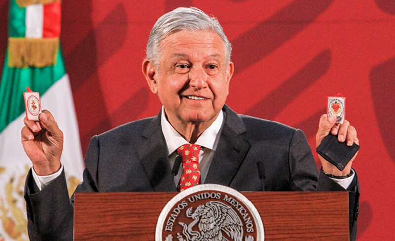El presidente López Obrador muestra dos tarjetas con los símbolos de Morena y el PT durante un discurso.