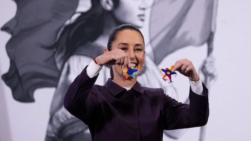 Claudia Sheinbaum sosteniendo una piñata en cada mano durante su conferencia matutina