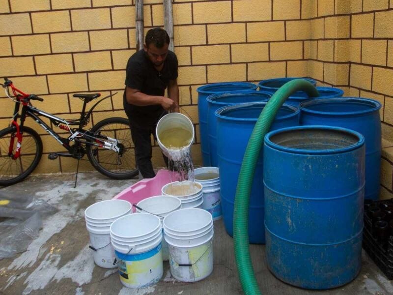 Un hombre llena cubetas con agua de un tanque en Venezuela