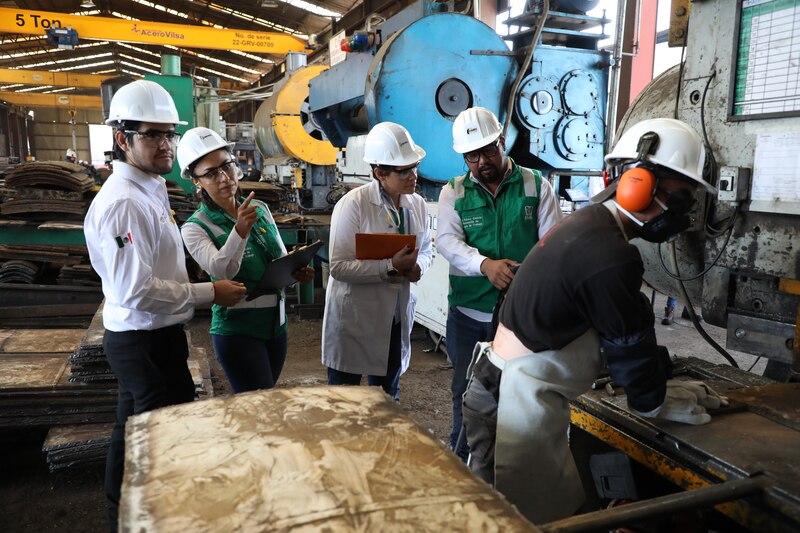 Trabajadores de una fábrica siderúrgica operan una máquina.