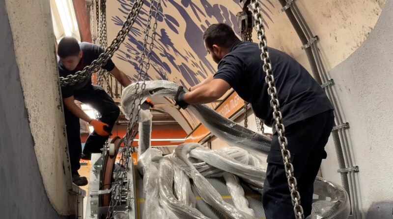 Dos hombres están reparando una escalera mecánica.