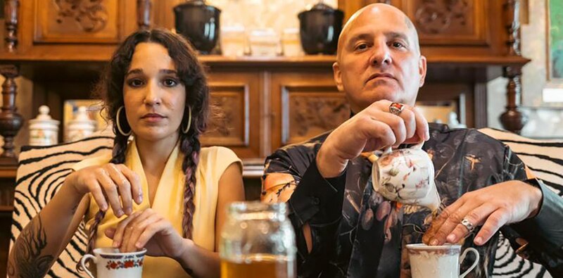 Dos personas tomando té en una mesa con una tetera y un tarro de miel.