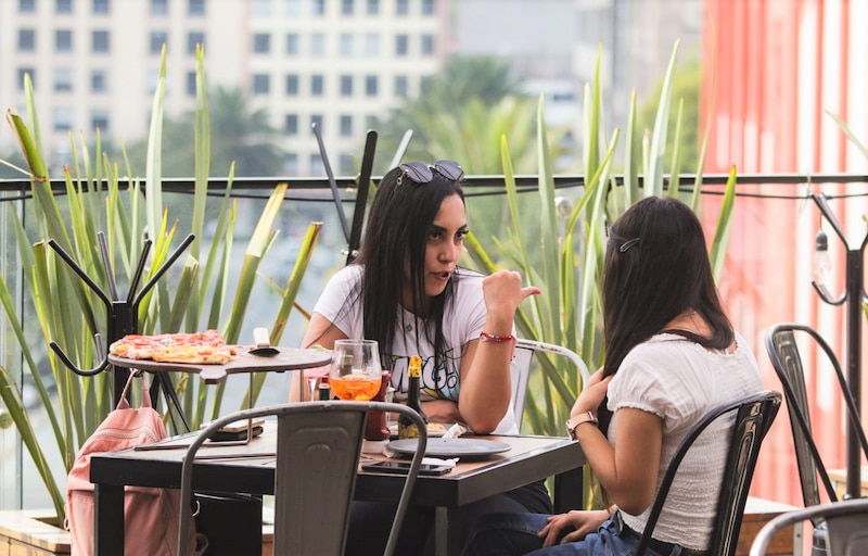 Dos mujeres jóvenes están sentadas en una mesa de un restaurante al aire libre.