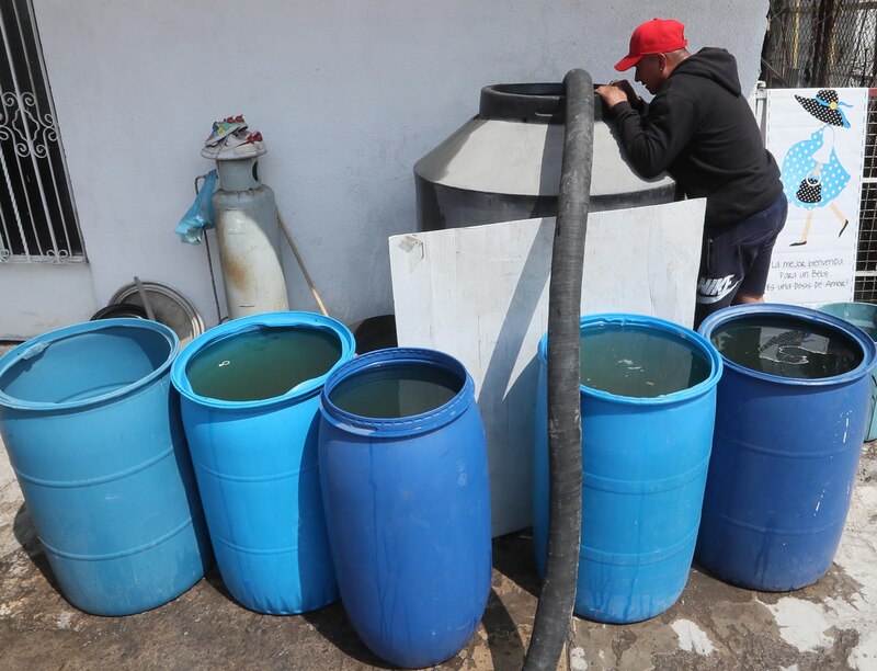 Un hombre llena de agua bidones azules