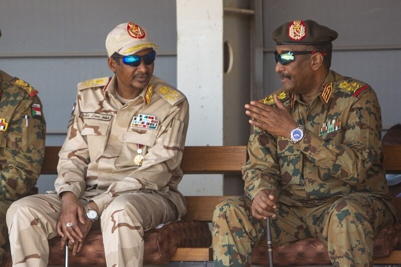 Dos generales en uniforme sentados en un banco hablan.