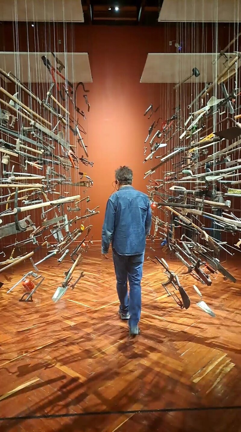 Un hombre camina por un pasillo con herramientas colgando del techo.