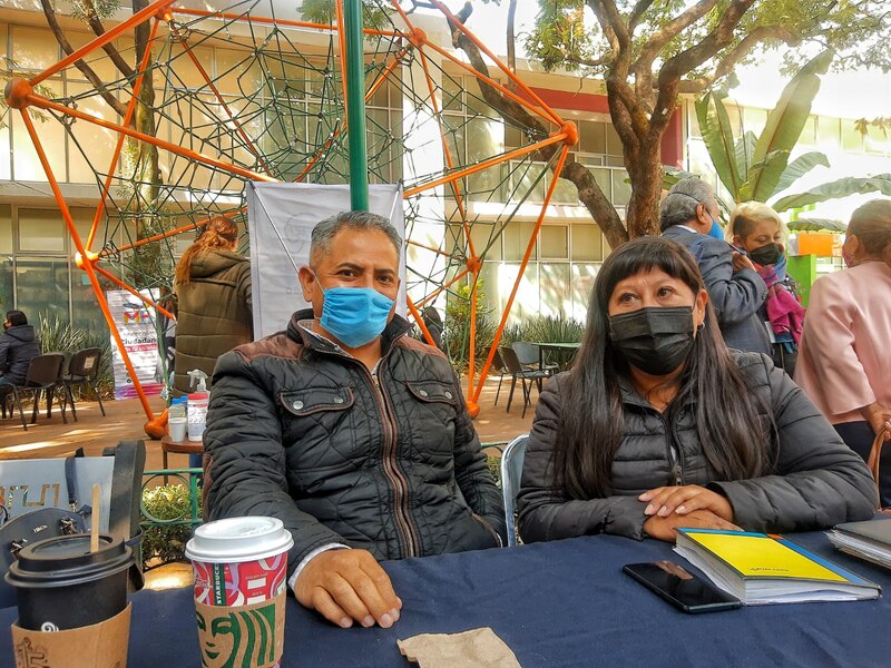 Dos personas sentadas en una mesa en el exterior con mascarillas.