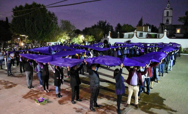 Un grupo de personas sostiene una tela morada en señal de protesta.
