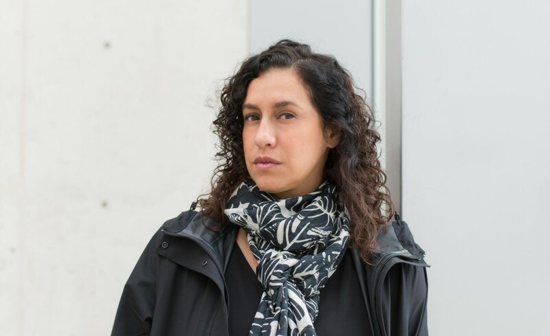 Retrato de una mujer joven con cabello castaño rizado y un abrigo negro