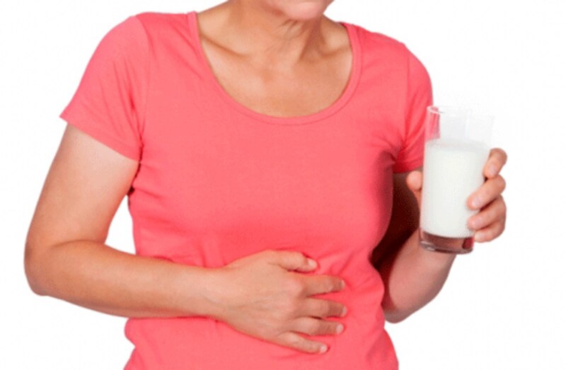 Mujer con dolor de estómago sosteniendo un vaso de leche
