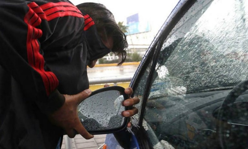 Un hombre limpia el espejo retrovisor de su coche bajo la lluvia