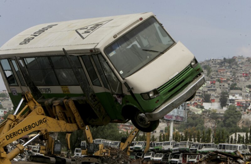Un autobús es izado por una grúa en un depósito de chatarra.
