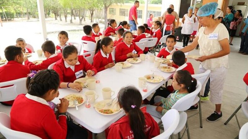 Niños y niñas reciben alimentos en un comedor escolar.