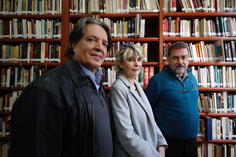 Tres personas sonríen en una biblioteca