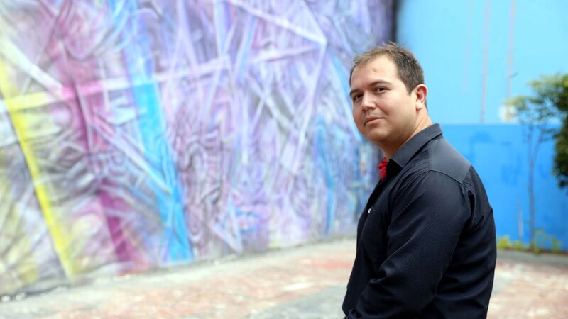 Un hombre posa delante de un mural de arte urbano.