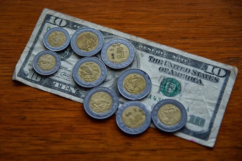 Monedas mexicanas y un billete de 10 dólares sobre una mesa de madera.