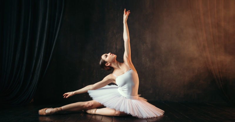 Una bailarina en tutú blanco realiza una pose de ballet en el suelo.