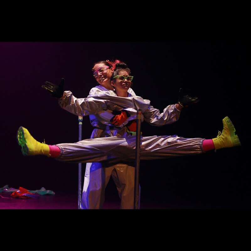 Dos mujeres en trajes espaciales realizan una acrobacia.