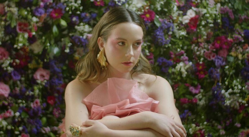 Mujer joven con vestido rosa frente a un muro de flores
