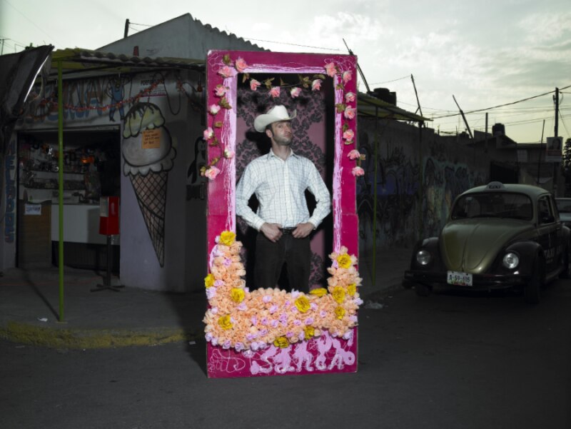 Un hombre con sombrero de vaquero posa en un marco de flores.