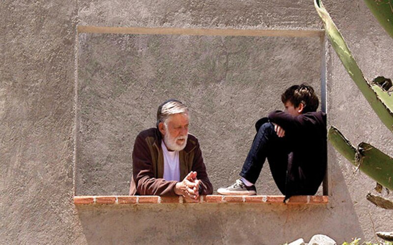 Un anciano y un niño conversan sentados en una ventana