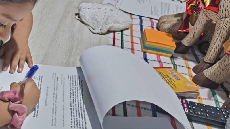 Niña sentada en el suelo escribiendo con un bolígrafo en una hoja de papel